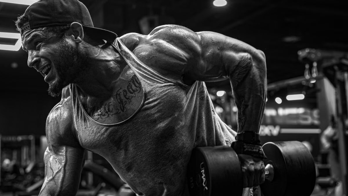 A muscular man lifting dumbbells intensely in a gym setting, showcasing strength and focus.